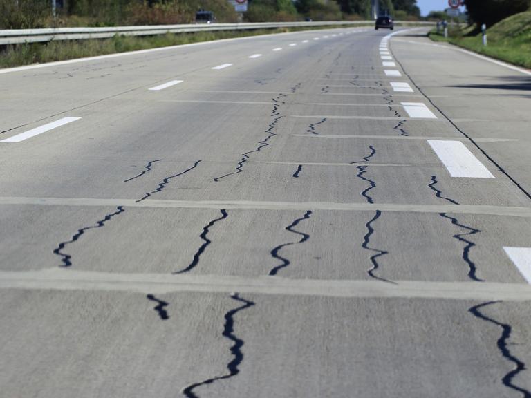 Autobahn mit Rissen in der Fahrbahn, im Hintergrund ein Auto