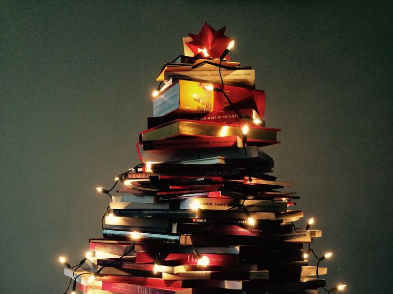 Beleuchtete Weihnachtsbeleuchtung auf einem zu einem Weihnachtsbaum geformten Bücherstapel.