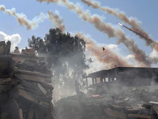 Palästinensische Gebiete, Gaza-Stadt: Raketen aus dem Gazastreifen werden über zerstörte Gebäude hinweg auf Israel abgefeuert.