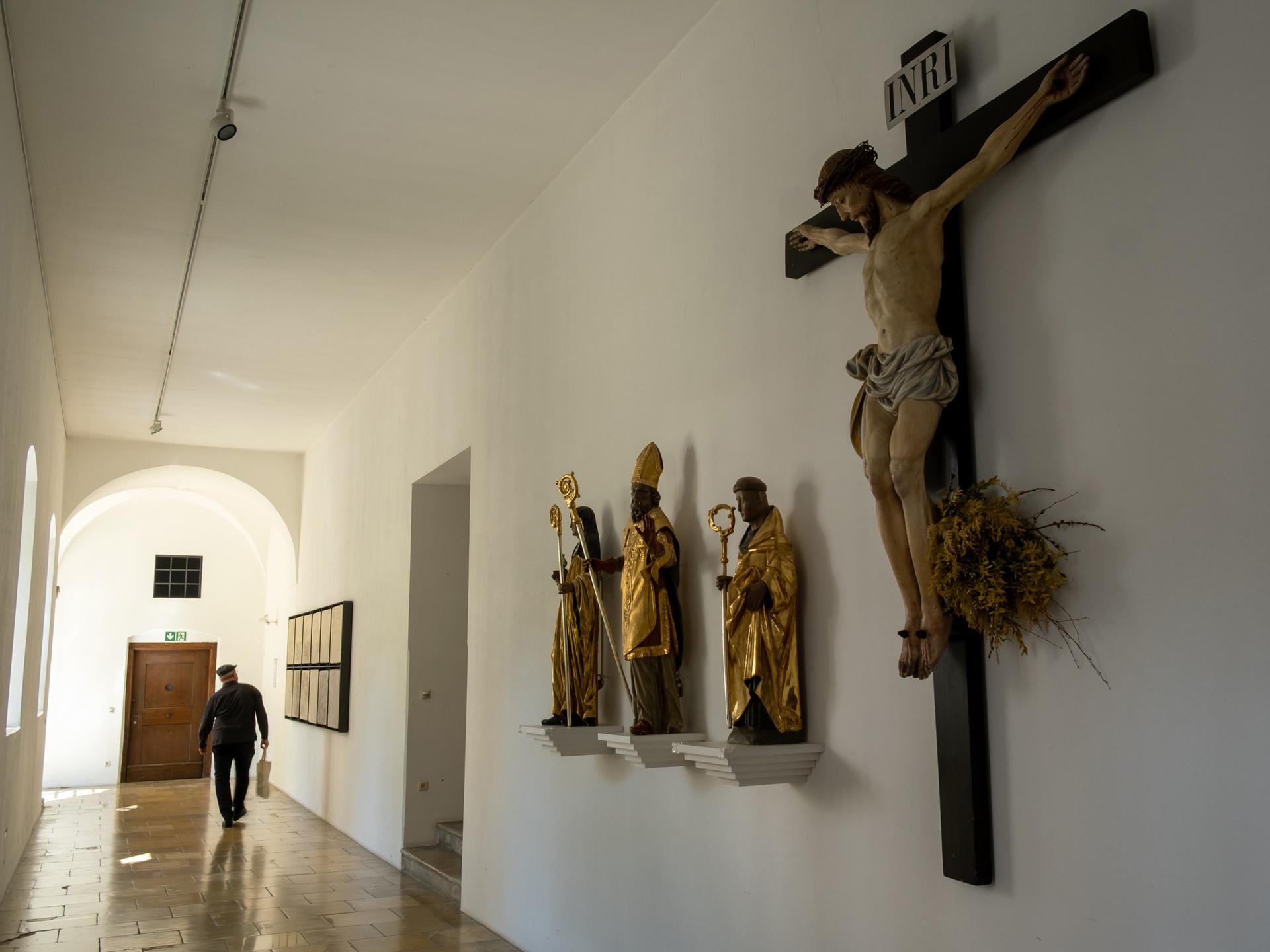 Im Gang eines Priesterseminars sind Statuen und ein Gekreuzigter zu sehen.