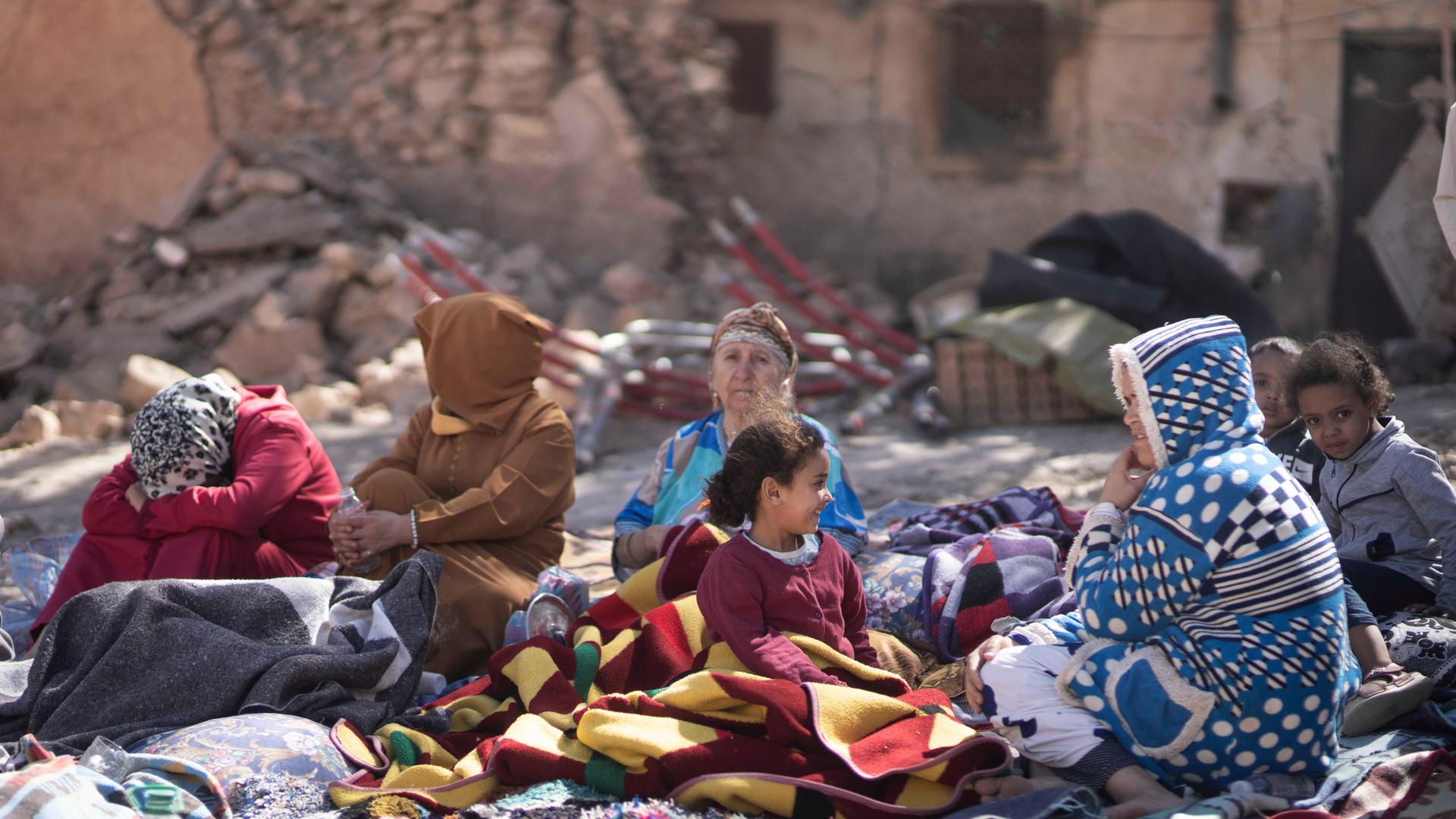 Familien mit ihren Kindern sitzen vor ihren zerstörten Häusern.