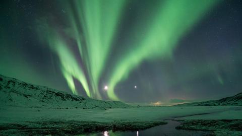 Grünleuchtende Nordlichter über einem bergigen Schneefeld in Island