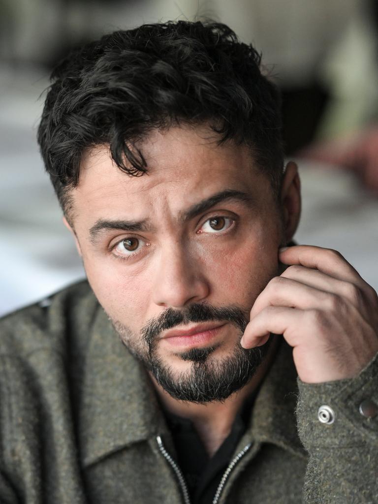 Der Schauspieler Aram Arami schaut offen in die Kamera und hält eine Hand an seinem Gesicht.