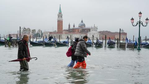Mehrere Personen waten durch Wasser auf der überfluteten Piazza San Marco in Venedig.