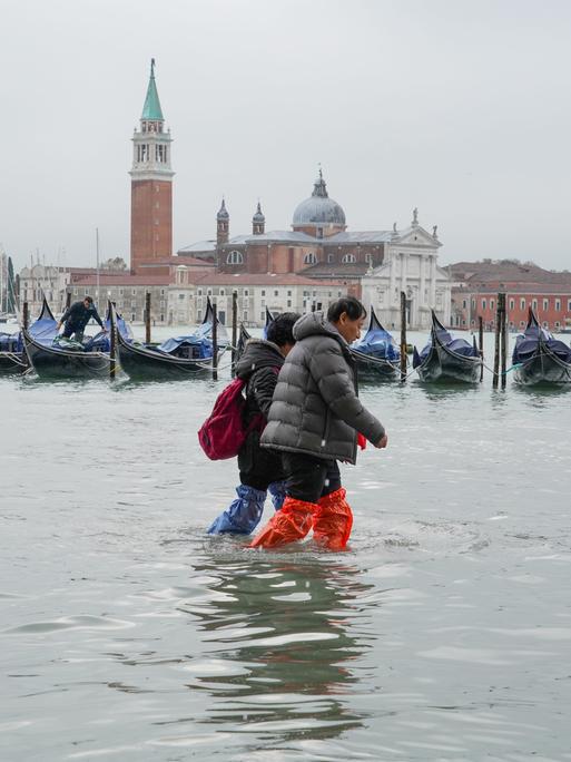 Mehrere Personen waten durch Wasser auf der überfluteten Piazza San Marco in Venedig.