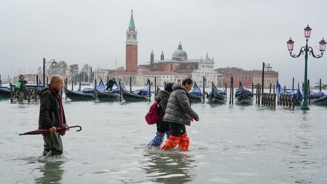 Mehrere Personen waten durch Wasser auf der überfluteten Piazza San Marco in Venedig.