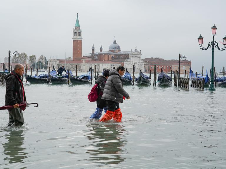 Mehrere Personen waten durch Wasser auf der überfluteten Piazza San Marco in Venedig.