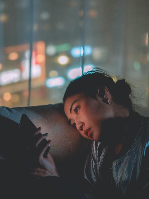 Frau die in der Nacht auf dem Sofa auf ihr Handy schaut. Frau die in der Nacht auf dem Sofa auf ihr Handy schaut.