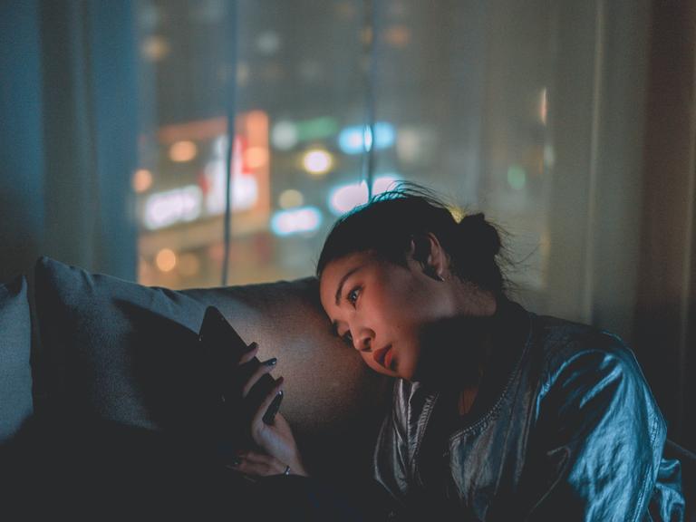 Frau die in der Nacht auf dem Sofa auf ihr Handy schaut. Frau die in der Nacht auf dem Sofa auf ihr Handy schaut.