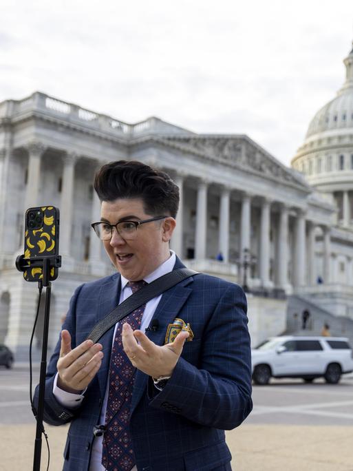 Ein Content Creator steht vor dem Kapitol und spricht in sein auf einem Stativ befestigten Smartphone.