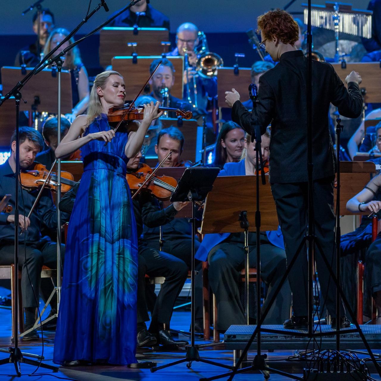 Die Geigerin steht vor dem Orchester und spielt innig auf ihrem Instrument. Die Geigerin steht vor dem Orchester und spielt innig auf ihrem Instrument.