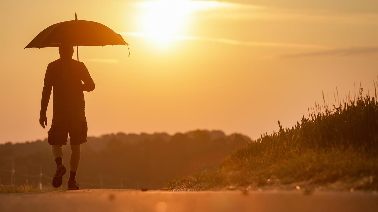 Hitze in Deutschland: Ein Mann geht mit einem Sonnenschirm spazieren.