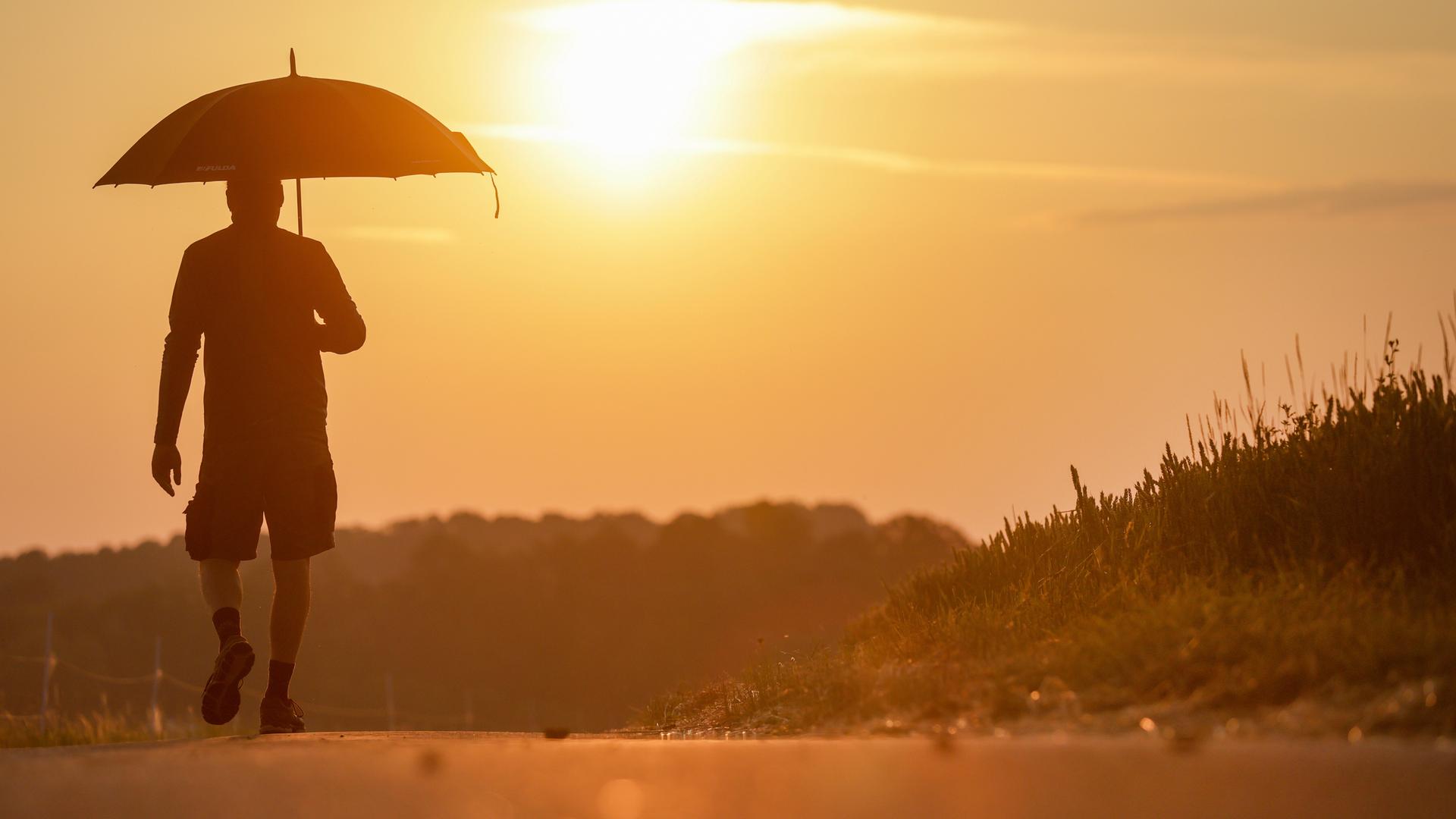 Hitze in Deutschland: Ein Mann geht mit einem Sonnenschirm spazieren.