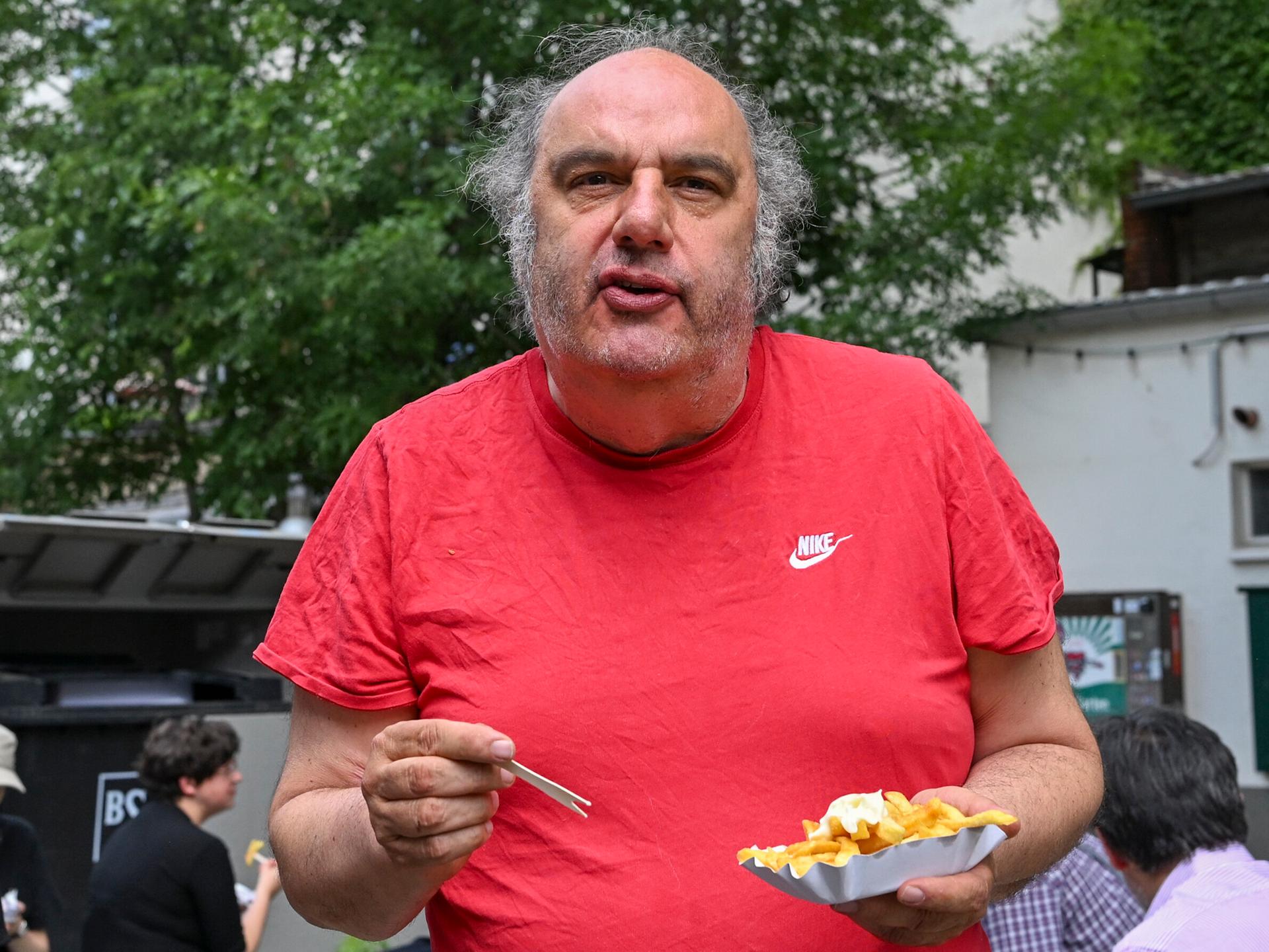 Matthias Lilienthal, der neue Intendant der Volksbühne, steht mit Pommes frites im Prater am Rande einer Pressekonferenz, wo er die Spielzeit 2026/27 der Volksbühne am Rosa-Luxemburg-Platz vorstellt.