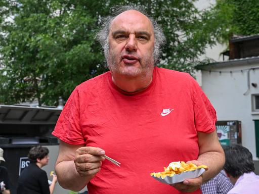 Matthias Lilienthal, der neue Intendant der Volksbühne, steht mit Pommes frites im Prater am Rande einer Pressekonferenz, wo er die Spielzeit 2026/27 der Volksbühne am Rosa-Luxemburg-Platz vorstellt.