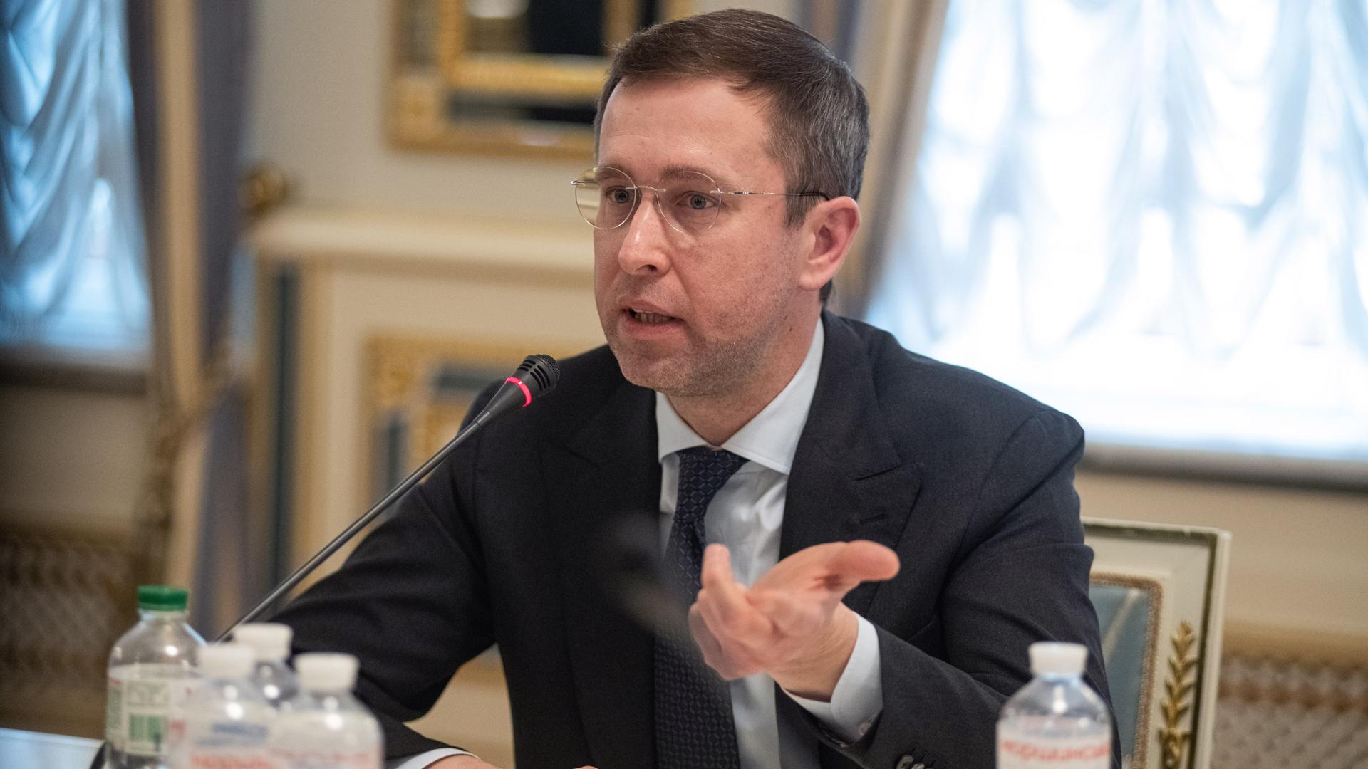 Serhii Koretskyi sitzt vor einem Mikrofon und gestikuliert mit der linken Hand.