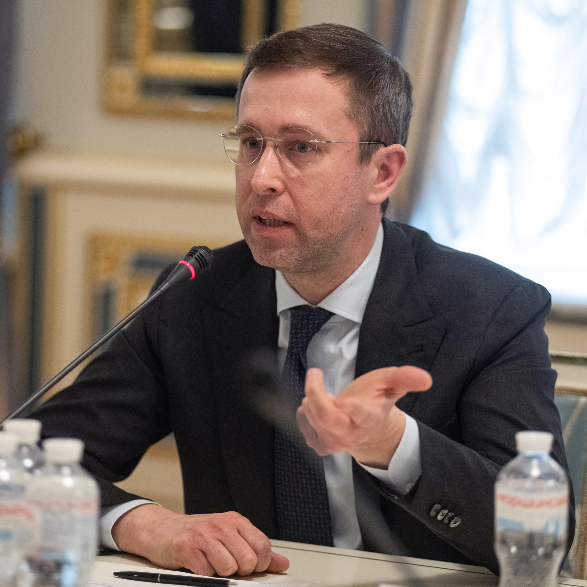 Serhii Koretskyi sitzt vor einem Mikrofon und gestikuliert mit der linken Hand.