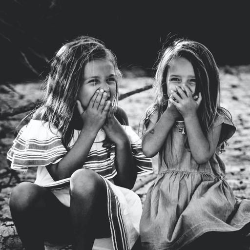 Zwei Mädchen sitzen auf einem Ast und kichern.
