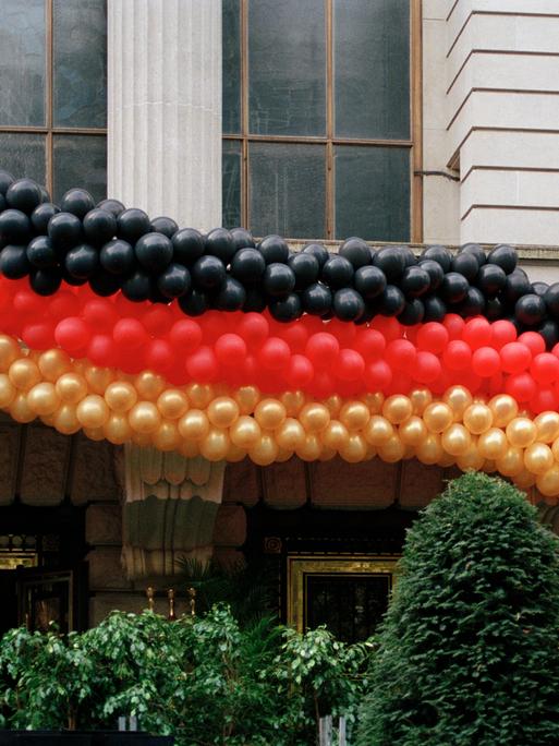 Eine Girlande aus Luftballons in den Farben der deutschen Flagge hängen an einer Hausfassade.
