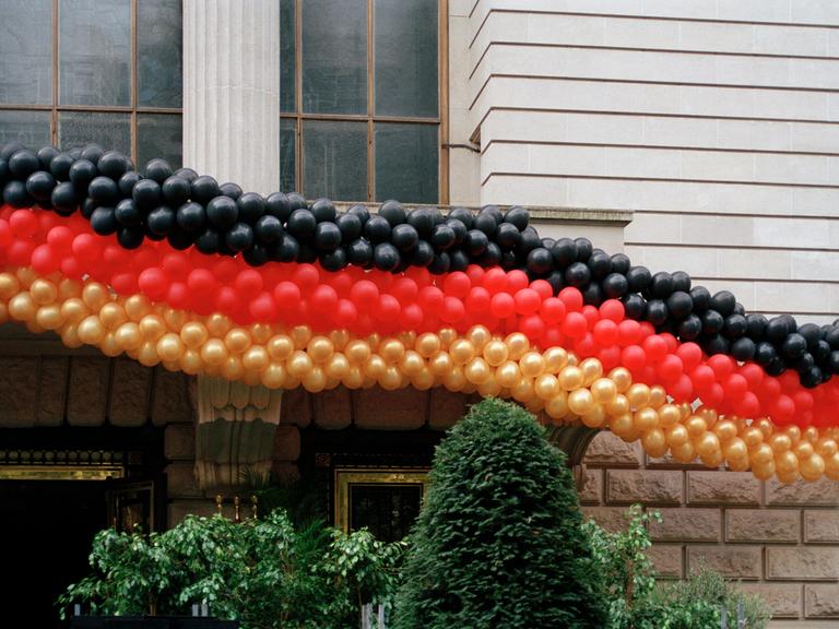 Eine Girlande aus Luftballons in den Farben der deutschen Flagge hängen an einer Hausfassade.