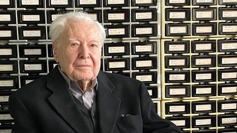 Ein alter Herr mit weißen Haaren sitzt mit gefaltenen Händen vor einem historischen Archivkatalog Ein alter Herr mit weißen Haaren sitzt mit gefaltenen Händen vor einem historischen Archivkatalog