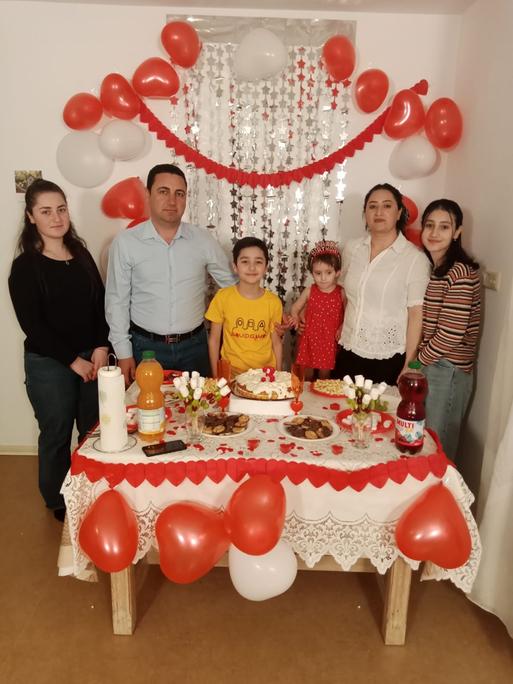 Familie Quasim, eine Familie mit Vater, Mutter und 4 Kindern vor einer festlich geschmückten Tafel, im Hintergrund Ballons