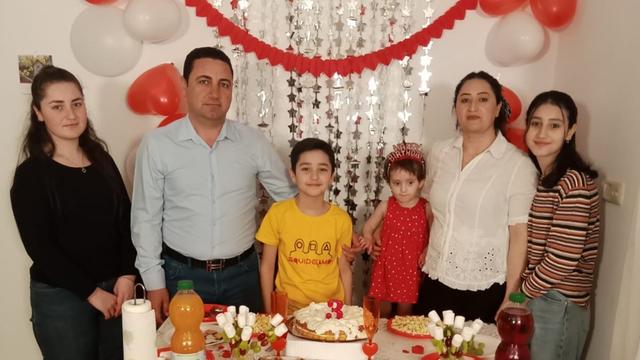 Familie Quasim, eine Familie mit Vater, Mutter und 4 Kindern vor einer festlich geschmückten Tafel, im Hintergrund Ballons