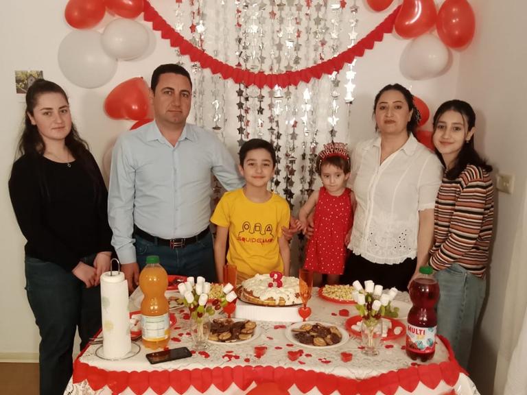 Familie Quasim, eine Familie mit Vater, Mutter und 4 Kindern vor einer festlich geschmückten Tafel, im Hintergrund Ballons