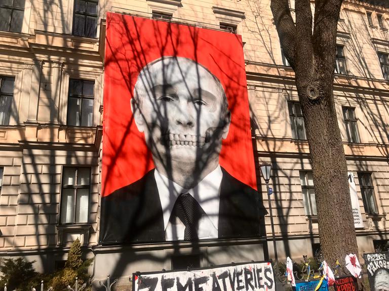 An der Fassade eines großen Gebäudes ist Putins Kopf auf rotem Hintergrund abgebildet, das Gebiß ähnelt einem Totenkopf.