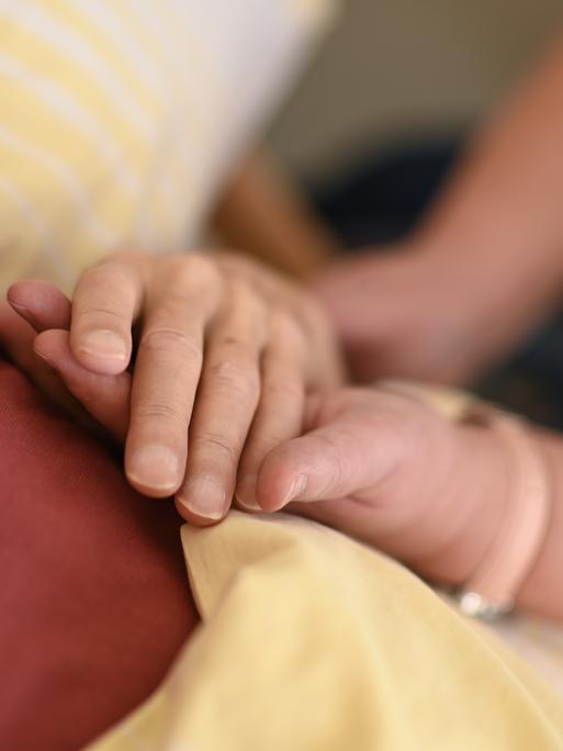 Eine Hospizmitarbeiterin hält die Hand eines todkranken Menschen, der im Hospiz im Bett liegt.