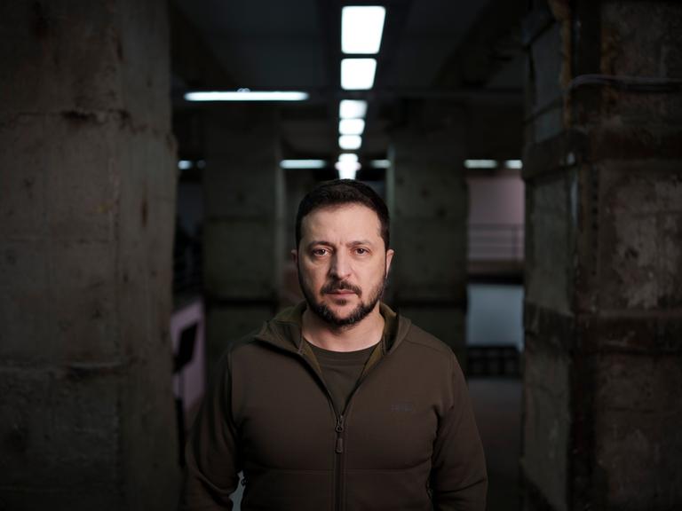 Der ukrainische Präsident Wolodymyr Selenskyj blickt in die Kamera; im Hintergrund sind Betonmauern und Neonröhren eines Bunkerraums zu erkennen.