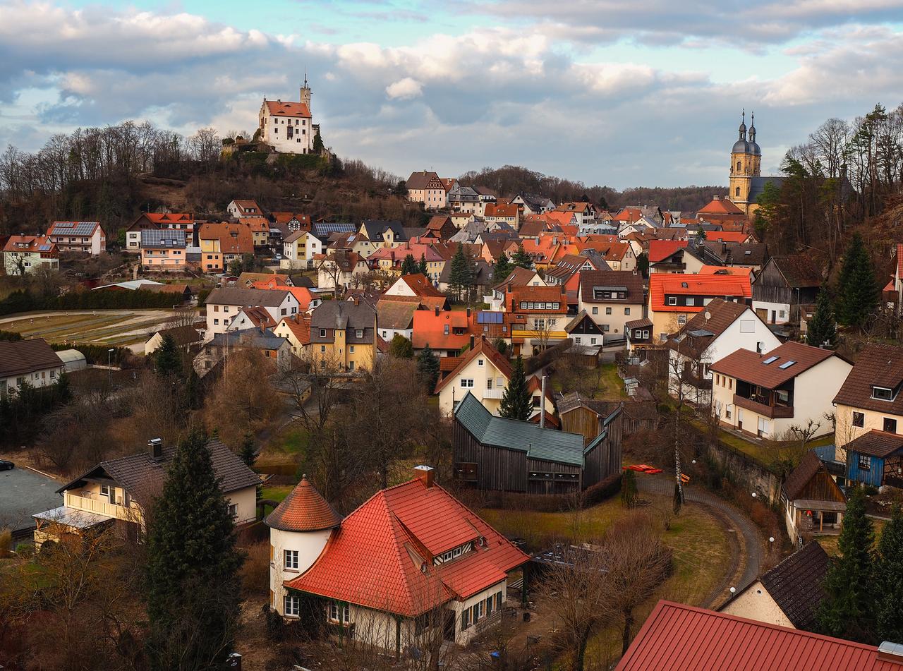 Ansicht des Markts Gößweinstein mit Kirchtürmen und einer kleinen Burg auf einem Hügel.