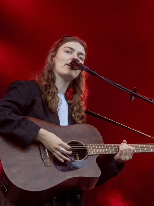 Musikerin Philine Sonny steht bei einem Festival auf der Bühne. Sie singt in ein Mikrofon und spielt dabei ihre Gitarre.