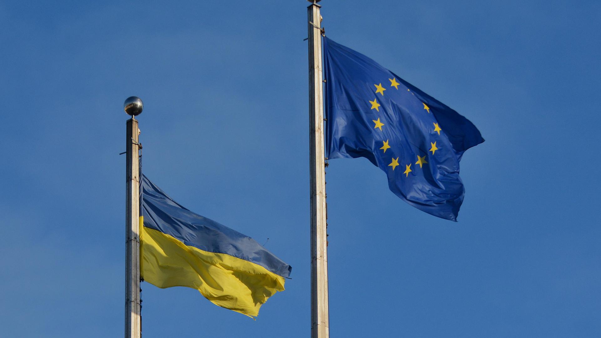 Die Flaggen der EU und der Ukraine wehen vor einem blauen Himmel.