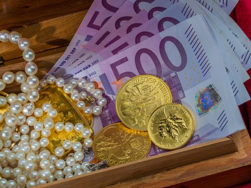 Gold in Münzen und Barren mit Schmuck auf rotem Samt. Symbolfoto für Reichtum