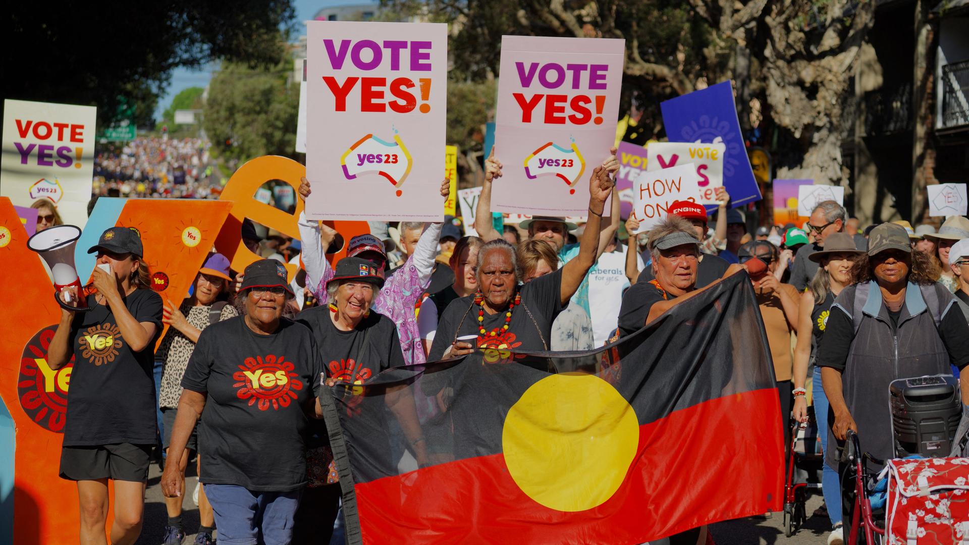 Australier demonstrieren für ein Referendum, dass indigenen Australiern mehr Rechte einräumt. Sie halten Plakate hoch mit der Aufschrift: "Vote Yes!"