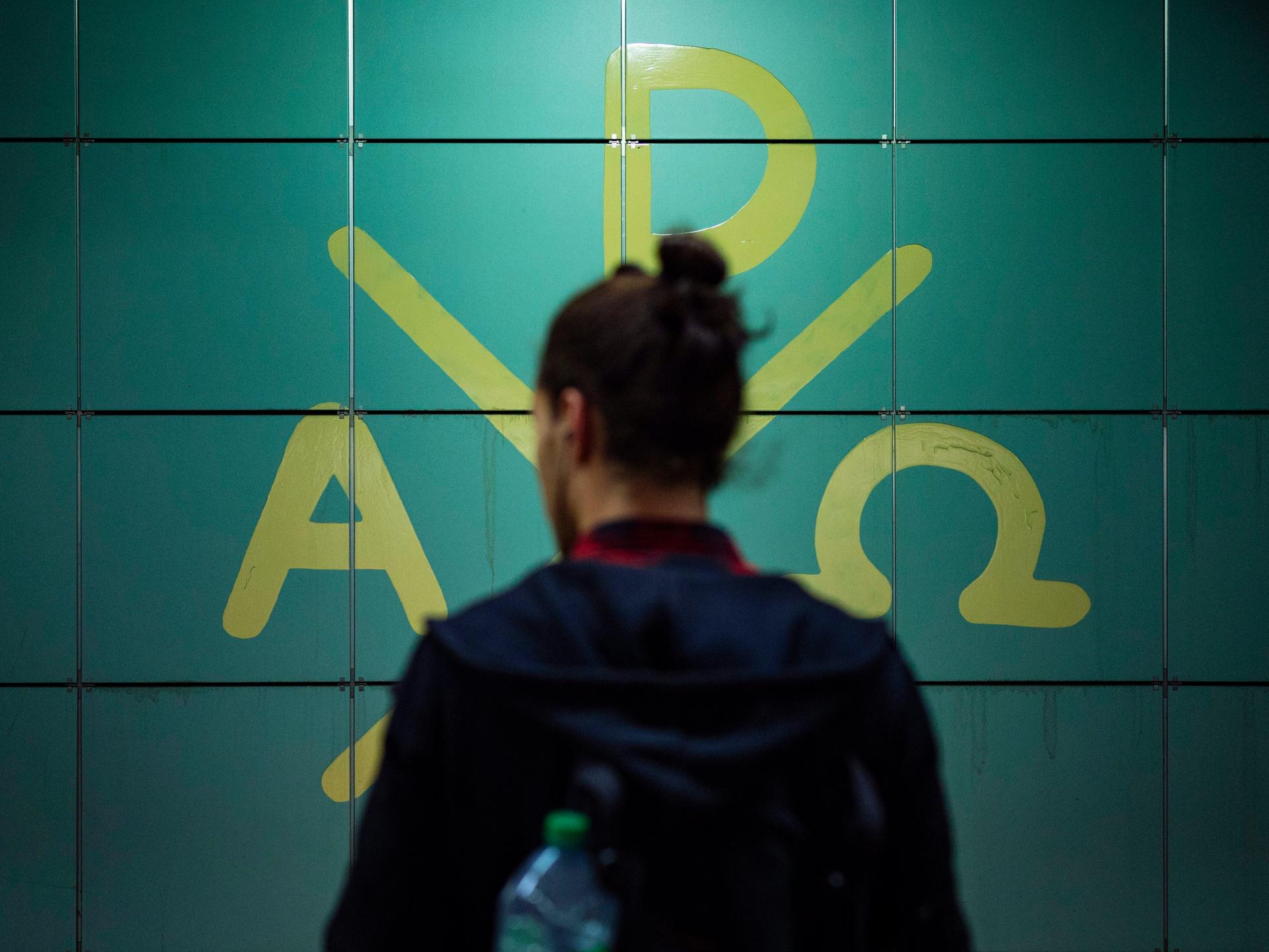 In einem Bahnhof steht ein Fahrgast vor den Symbolen des Christentums. Der Mensch ist nur von hinten angebildet, sein Gesicht ist nicht zu erkennen.