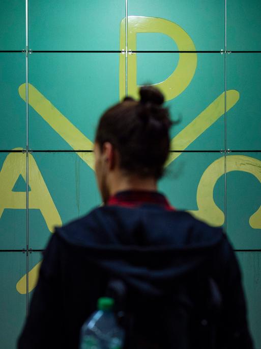 In einem Bahnhof steht ein Fahrgast vor den Symbolen des Christentums. Der Mensch ist nur von hinten angebildet, sein Gesicht ist nicht zu erkennen.