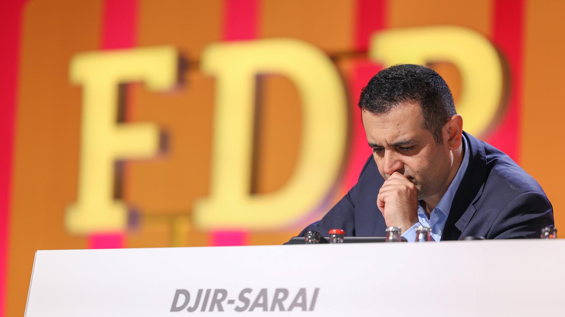 Bijan Djir-Sarai, FDP-Generalsekretär sitzt beim Abschluss des Bundesparteitags an einem Rednerpult. Im Hintergrund sind die Buchstaben FDP an der Wand zu sehen. Am Rednerpult steht der Name des Generalsekretärs. Er stützt sich mit dem Kinn auf eine Hand und sieht nach unten.