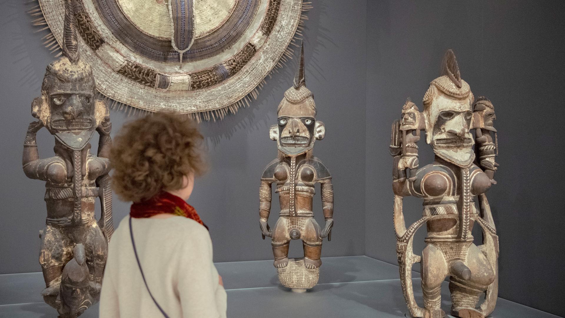 Eine Besucherin des Humboldt Forums steht vor afrikanischen Skulpturen und schaut sie sich an.