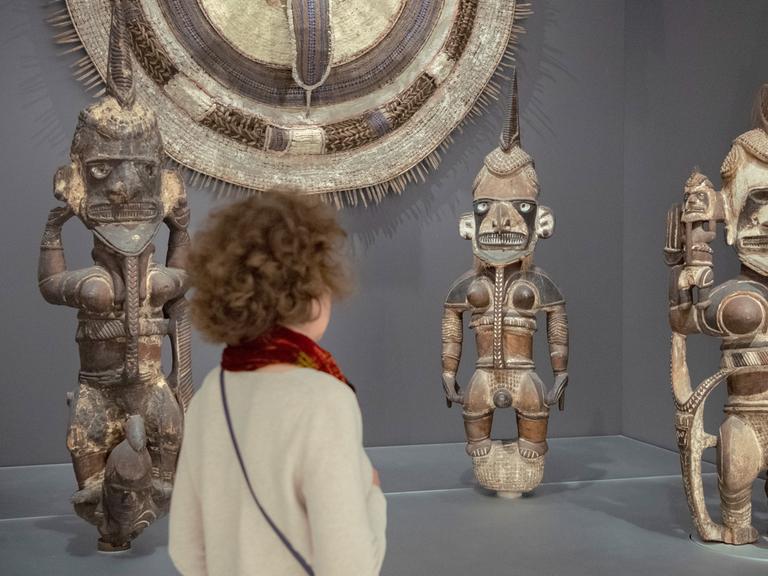 Eine Besucherin des Humboldt Forums steht vor afrikanischen Skulpturen und schaut sie sich an.
