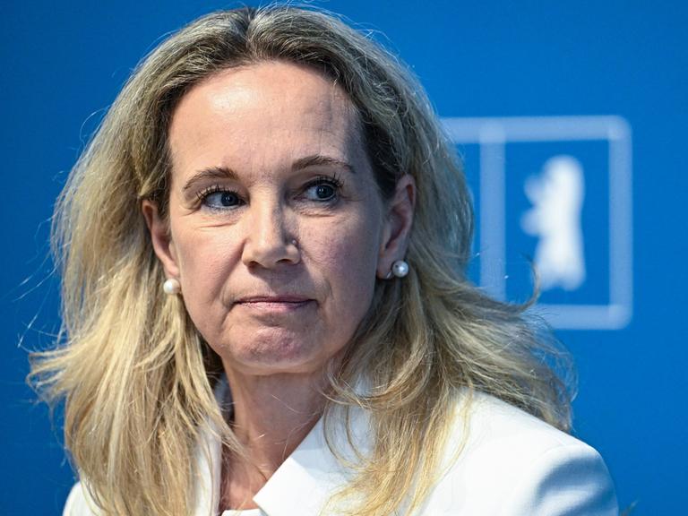 Sarah Wedl-Wilson sitzt auf einem Podium vor einer blauen Wand auf der "Berlin" steht