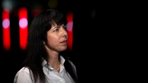 Elif Eralp , Spitzenkandidatin der Partei Die Linke in Berlin, ist bis zu den Schultern abgebildet. Sie trägt eine weiße Bluse, die schwarzen langen Haare offen und roten Lippenstift. Sie schaut an der Kamera vorbei.