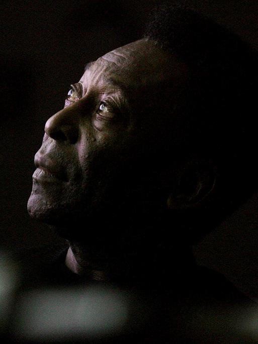 Pelé schaut mit ernstem Blick nach oben, der Rand seines Kopfes verschwimmt mit dem schwarezen Hintergrund. 