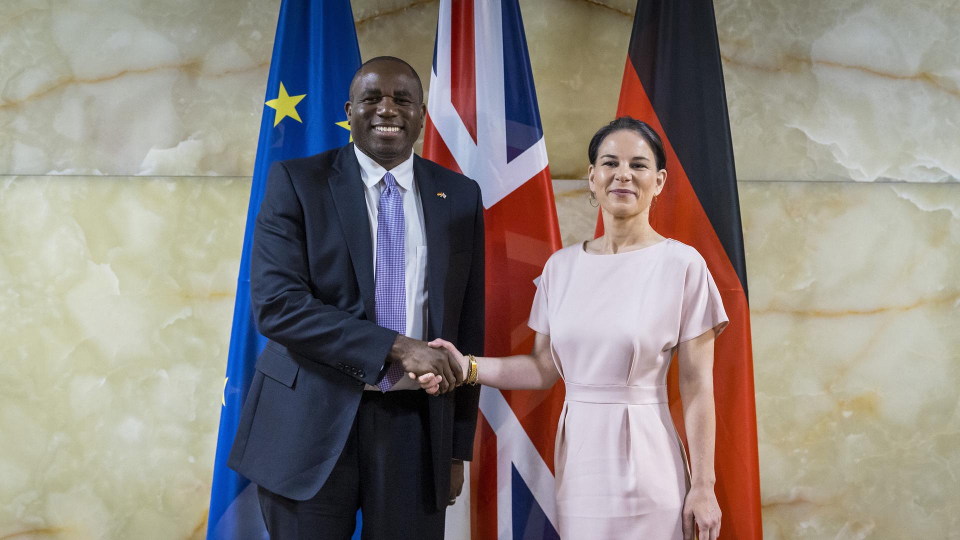 Der neue britische Außenminister Lammy und die deutsche Außenministerin Baerbock stehen vor der britischen, deutschen und europäischen Fahne und schütteln sich die Hände. 