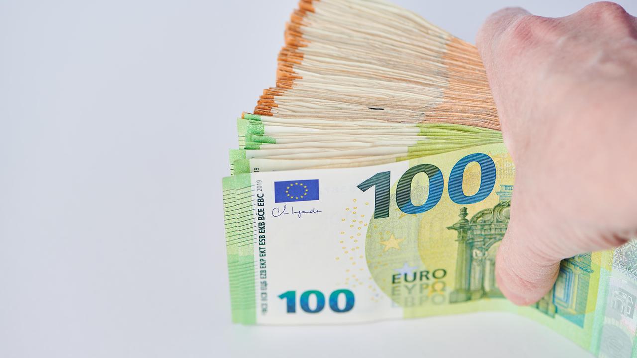 Eine Hand hält eine Bündel Euro-Banknoten vor einem hellen Hintergrund zwischen Daumen und den übrigen Fingern.