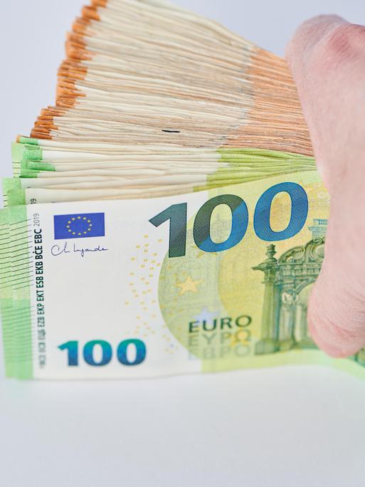 Eine Hand hält eine Bündel Euro-Banknoten vor einem hellen Hintergrund zwischen Daumen und den übrigen Fingern. Eine Hand hält eine Bündel Euro-Banknoten vor einem hellen Hintergrund zwischen Daumen und den übrigen Fingern.