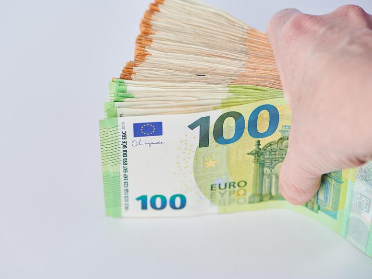 Eine Hand hält eine Bündel Euro-Banknoten vor einem hellen Hintergrund zwischen Daumen und den übrigen Fingern. Eine Hand hält eine Bündel Euro-Banknoten vor einem hellen Hintergrund zwischen Daumen und den übrigen Fingern.