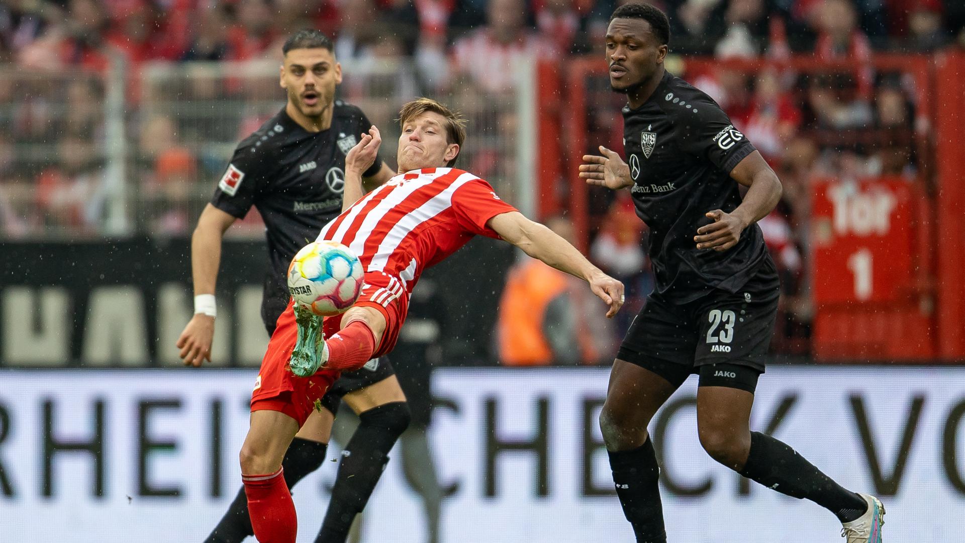 Zwei Spieler des VfB Stuttgart kämpfen gegen einen gegnerischen Spieler von Union Berlin um den Ball.