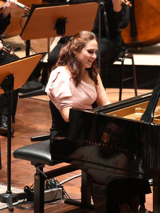 Blick auf die am Flügel sitzende und dabei strahlende Pianistin während ihres Auftrittes mit dem Mahler Chamber Orchestra.